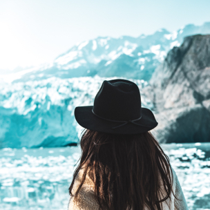 A woman wearing a hat staring at some ice-bergs.